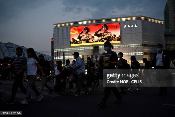 This photo taken on May 18, 2021 shows people walking along a street as military propaganda is displayed on a giant screen in Beijing. - China is...