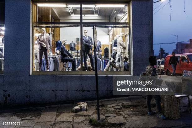 Man holds a basket of merchandise for sale at a corner of a street in the Piazza area of Addis Ababa, on June 17, 2021 as stray dog sleeps under a...