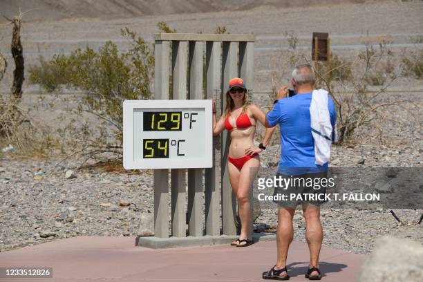 John Gillette takes a photo of Sarah Null as she stands in a swimsuit next to a thermometer displaying temperatures of 129 Degrees Fahrenheit at the...