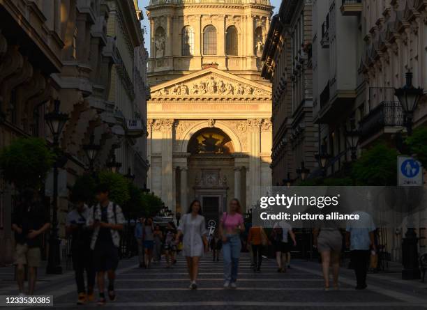 June 2021, Hungary, Budapest: Passers-by walk along a pedestrian street in front of St. Stephen's Basilica in the Pest district of the city in the...