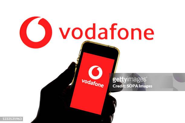 In this photo illustration a Vodafone logo seen displayed on a smartphone with a Vodafone logo in the background.