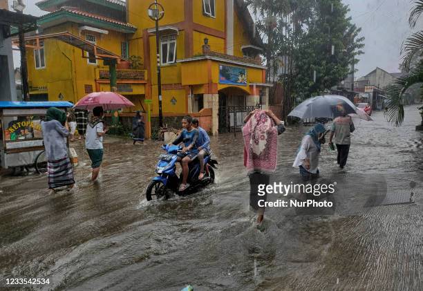 Commuters make their way along a waterlogged street after heavy rains in Bogor Regency, West Java, Indonesia on June 18, 2021.