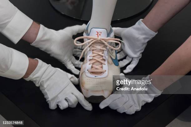 Staff members adjust a Nike sneaker which is part of Roger Federer's signed champion outfit and racket from 2009 French Open during a photo call for...