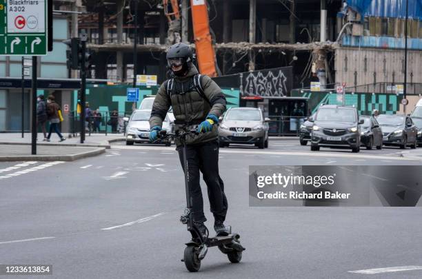 An eScooter rider wearing goggles over his face and a helmet protecting his head, speeds ahead of traffic, on 22nd June 2021, in London, England.