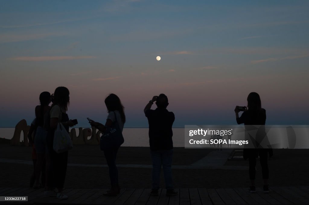 People watch and take pictures of the moon illuminated...