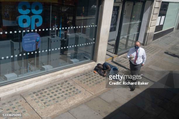 Wealthier man carrying his lunch, walks past a male lying on the pavement outside a branch of the Co-Op bank on the Strand, on 23rd June 2021, in...