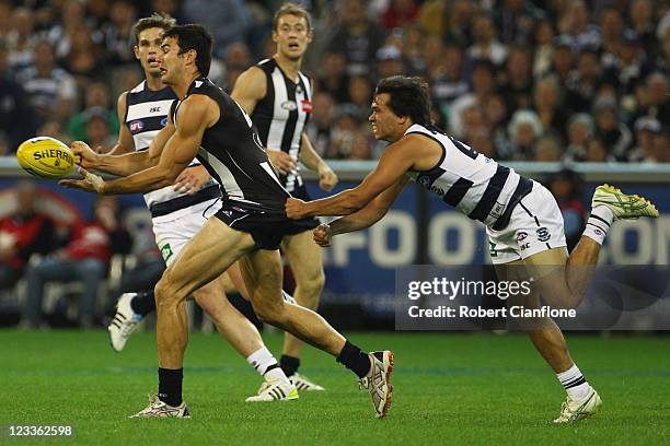 Chris Tarrant handballs as Allen Christensen of the Cats attempts to tackle during the round 24 AFL match between the Collingwood Magpies and the...