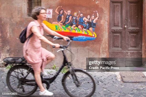 Woman biking passes by the wall with a mural made by Italian street artist Harry Greb named "Enjoy - Tutti al mare" via dei Montecatini in Rome...