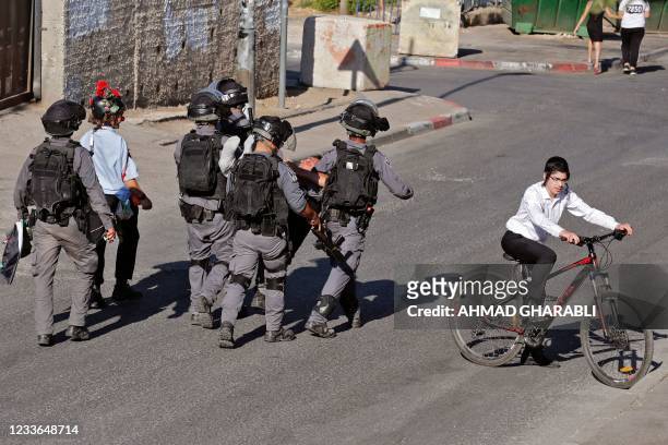 An Ultra-Orthodox Jewish boy rides his bicycle as Israeli security forces arrest an activist near a police checkpoint at the entrance of the Sheikh...