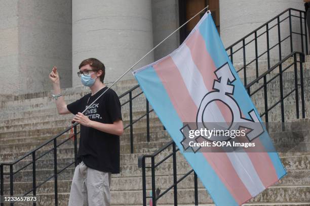 Protester holds the trans flag and snaps in solidarity with other speakers, during the demonstration. Transgender rights advocates stood outside of...