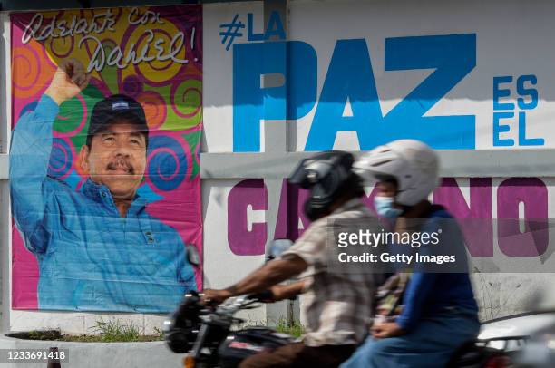 Couple in a motorcycle rides in front of a billboard with a picture of Nicaraguan President Daniel Ortega at Ministry of Family Economy on June 27,...