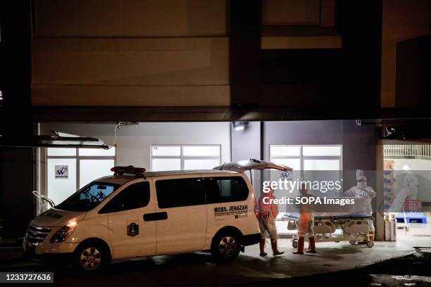 Health workers wearing Personal Protective Equipment push a coffin containing the body of a covid-19 victim inside the Wisma Atlet Covid- Indonesia...