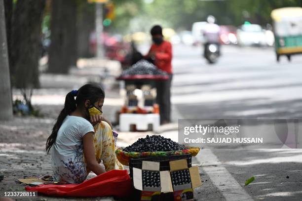 Girl selling fresh jamun waits for customers at a roadside stall in New Delhi on June 30, 2021.