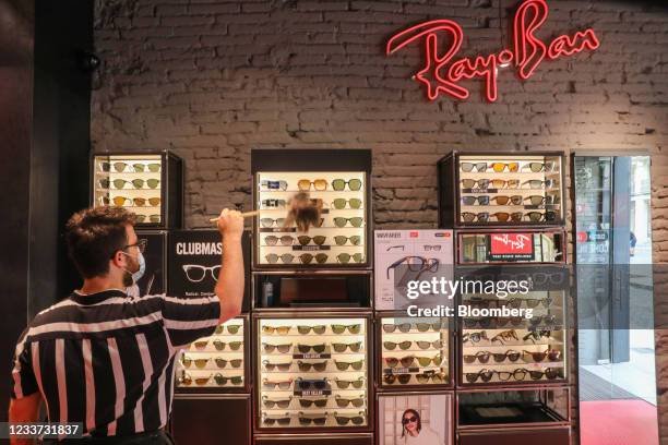 Worker dusts a display of Ray-Ban sunglasses, manufactured by EssilorLuxottica SA, inside a Ray-Ban store, in Barcelona, Spain, on Wednesday, June...