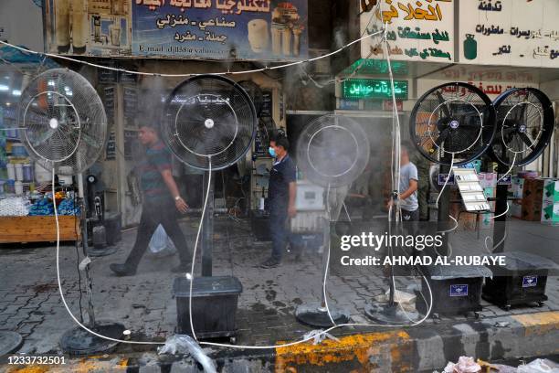 People walk past fans spraying air mixed with water vapour deployed by donors to cool down pedestrians along a street in Iraq's capital Baghdad on...