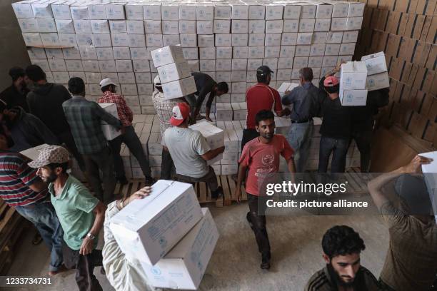 June 2021, Syria, Bab Al-Hawa: Syrians store World Food Programme humanitarian aid after unloading the transporting trucks that entered earlier from...