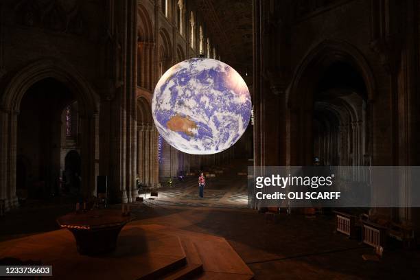 Member of staff stands beneath British artist Luke Jerram's installation 'Gaia', a 7 meter replica of planet Earth, suspended in the nave of Ely...