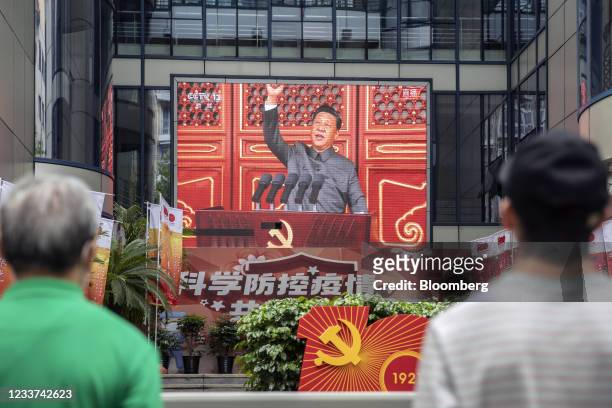 Pedestrians watch a screen showing a live news broadcast of Chinese President Xi Jinping speaking at a ceremony marking the centenary of the Chinese...