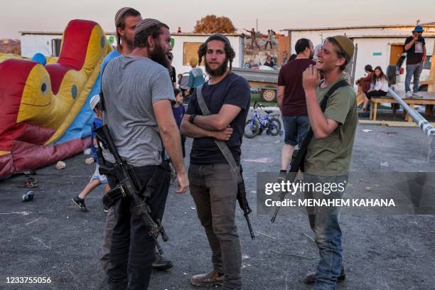 Israeli settlers carrying assault rifles gather next to an inflatable children's attraction in the newly-established wildcat outpost of Eviatar near...