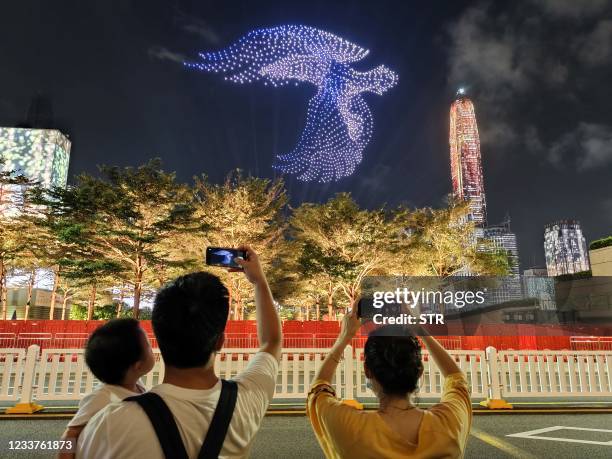 This photo taken on July 1, 2021 shows people taking photos on a bird formed by drones during a show marking the 100th anniversary of the Chinese...