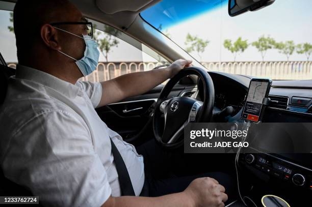 Driver uses the Didi Chuxing app on his smartphone while driving along the street in Beijing on July 2, 2021.