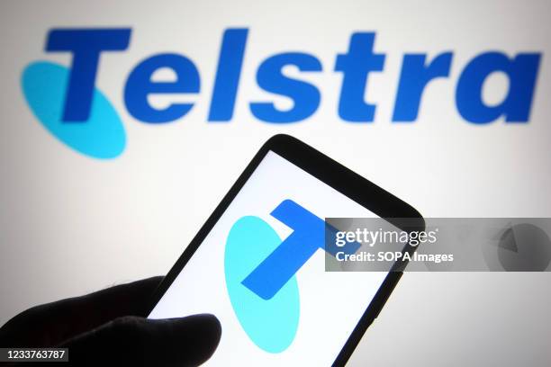 In this photo illustration a Telstra logo is seen on a smartphone and a pc screen.