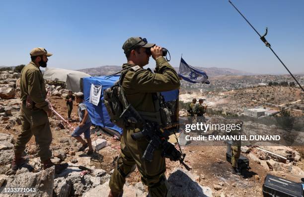 Israeli soldiers observe the Palestinian village of Beita with binoculars as settlers evacuate the newly-established wildcat outpost of Eviatar in...