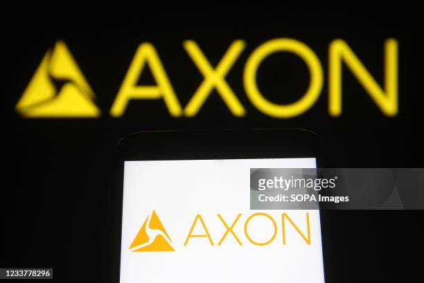 In this photo illustration an Axon Enterprise logo is seen on a smartphone and a pc screen.