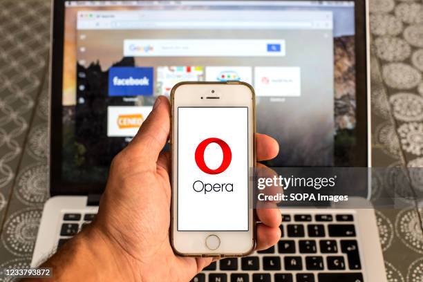 In this photo illustration, an Opera web browser logo seen displayed on a smartphone in front of a laptop.