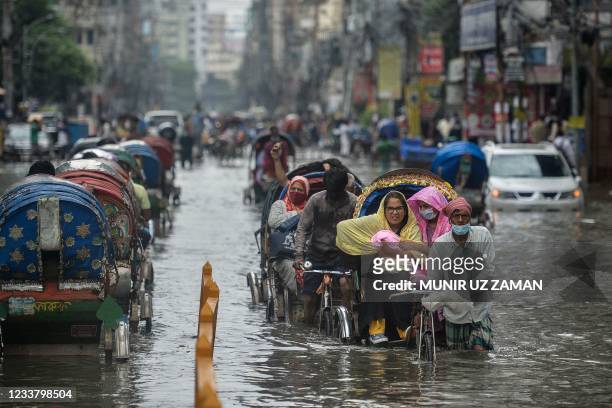 Cycle rickshaw pullers wade through a waterlogged street carrying their passengers after a heavy downpour in Dhaka on July 4, 2021.