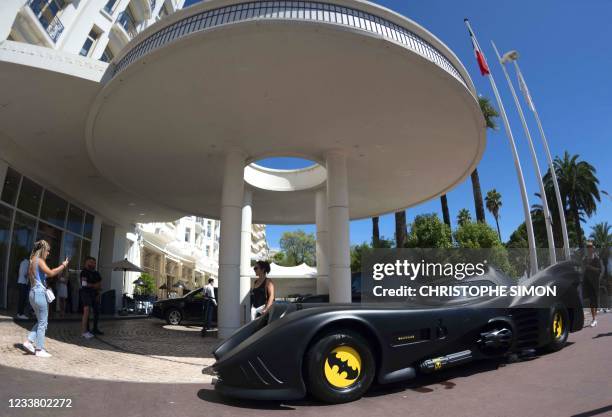 Woman poses for a photo next to a Batmobile, parked in front of the Martinez palace in Cannes, Southeastern France, on July 4 two days before the...