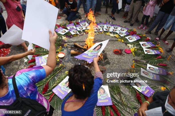 July 2021, Honduras, Tegucigalpa: People place small posters depicting Honduran environmental activist Berta Caceres next to a fire as they wait...