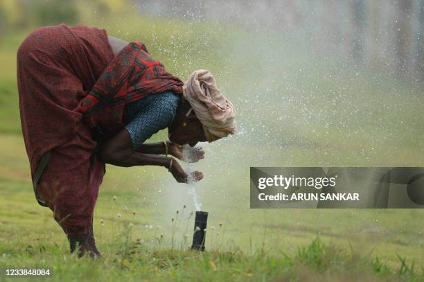 Woman washes her face with water from a sprinkler during a hot summer day in Chennai on July 7, 2021.