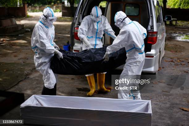 Volunteers wearing personal protective equipment carry the body of a person who died from the Covid-19 coronavirus into a coffin before the cremation...