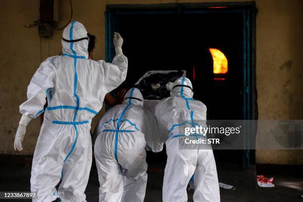 Volunteers wearing personal protective equipment push the body of a person who died from the Covid-19 coronavirus into a cremation chamber in...