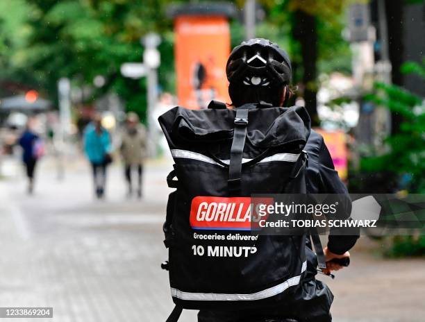 Bicycle courier of grocery delivery company "Gorillas" wears a backpack with the logo of the startup on his way to deliver purchases in Berlin on...