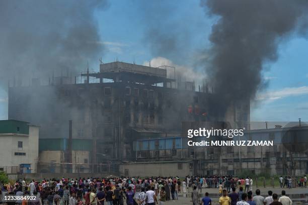 Onlookers watch as smoke bellows from a massive fire that broke out a day before in a beverage and food factory in Rupganj in the district...