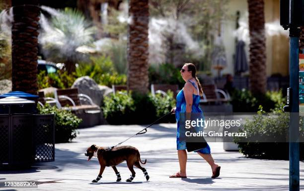 Woman walks her dogs whos wearing booties to protect his paws from the hot pavement near downtown misters in 110 degree temperatures on July 8, 2021...