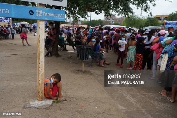 Young boy rests next to a long line of people waiting for clothes, food and supplies in a makeshift migrant camp in the border town of Reynosa,...