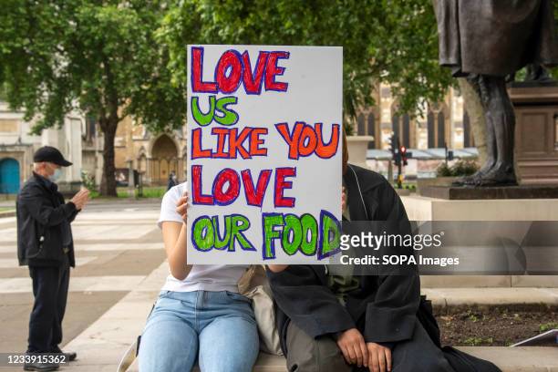 Protesters with a placard saying 'Love us like you love our food' take part during a Stop Asian Hate protest at Parliament Square in London....