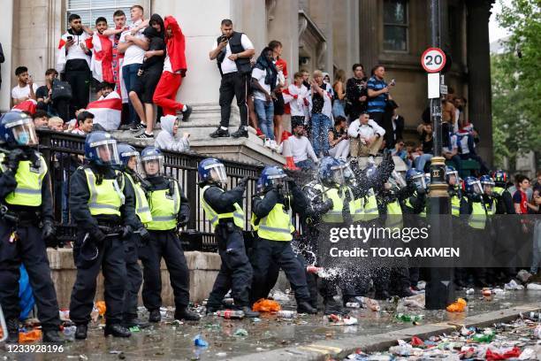 Line of police officers are the target of beer can throwers as England supporters stand around the edges of Trafalgar Square during a live screening...