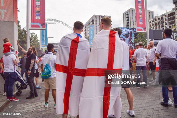 Football fans wrapped in English flags stand outside Wembley Stadium ahead of the England v Italy Euro 2020 final.