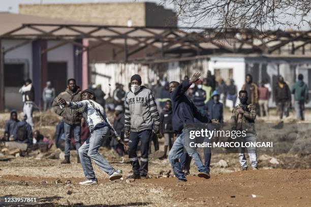 Disgruntled residents throw rocks as they confront police officers at the entrance of a partially looted mall in Vosloorus, on July 13, 2021. -...