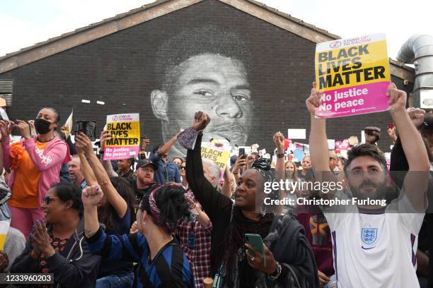 People hold Black Lives Matter posters aloft as they gather at the newly repaired mural of England footballer Marcus Rashford by the artist known as...