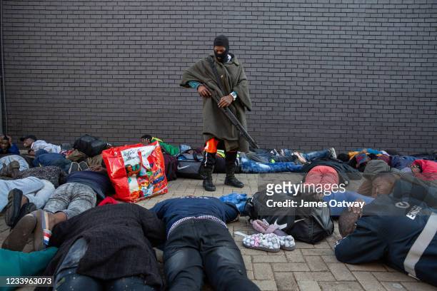 Policeman guards a group of suspected looters who were apprehended at a shopping centre on July 13, 2021 in Vosloorus, Johannesburg, South Africa....
