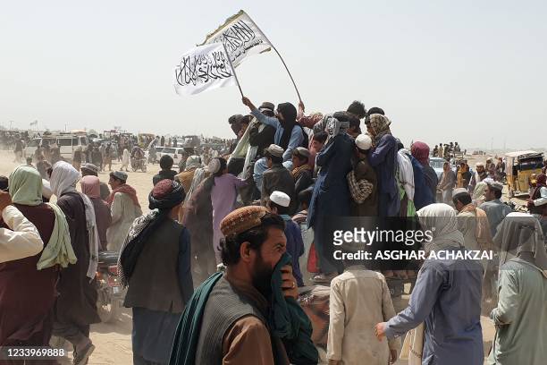 People wave Taliban flags as they drive through the Pakistani border town of Chaman on July 14 after the Taliban claimed they had captured the Afghan...