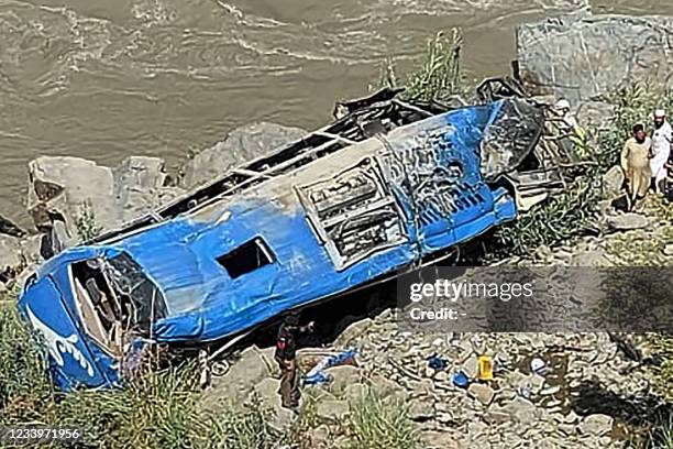 People stand next to a wreck after a bus plunged into a ravine following a bomb attack, which killed 12 people including 9 Chinese workers, in...