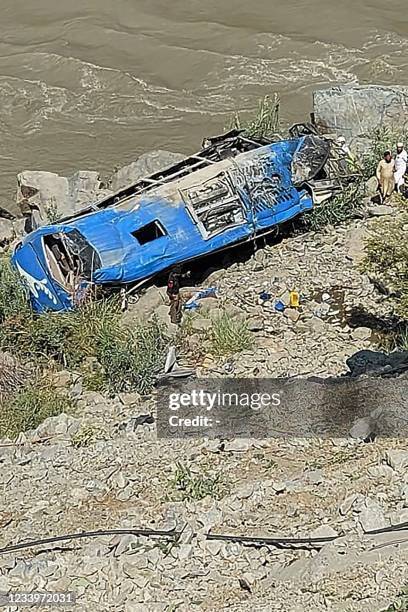 People stand next to a wreck after a bus plunged into a ravine following a bomb attack, which killed 12 people including 9 Chinese workers, in...