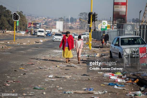 Woman and a young girl walk through debris on July 14, 2021 in Vosloorus, Johannesburg, South Africa. South Africa has deployed the military to quell...