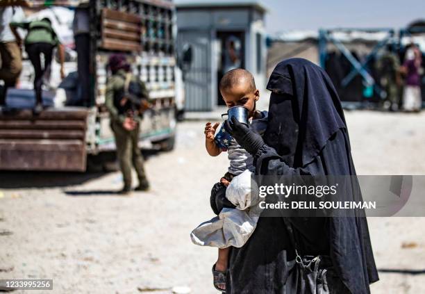 Syrian woman helps a child to drink as she waits with family members inside the Kurdish-run al-Hol camp, which holds relatives of suspected Islamic...
